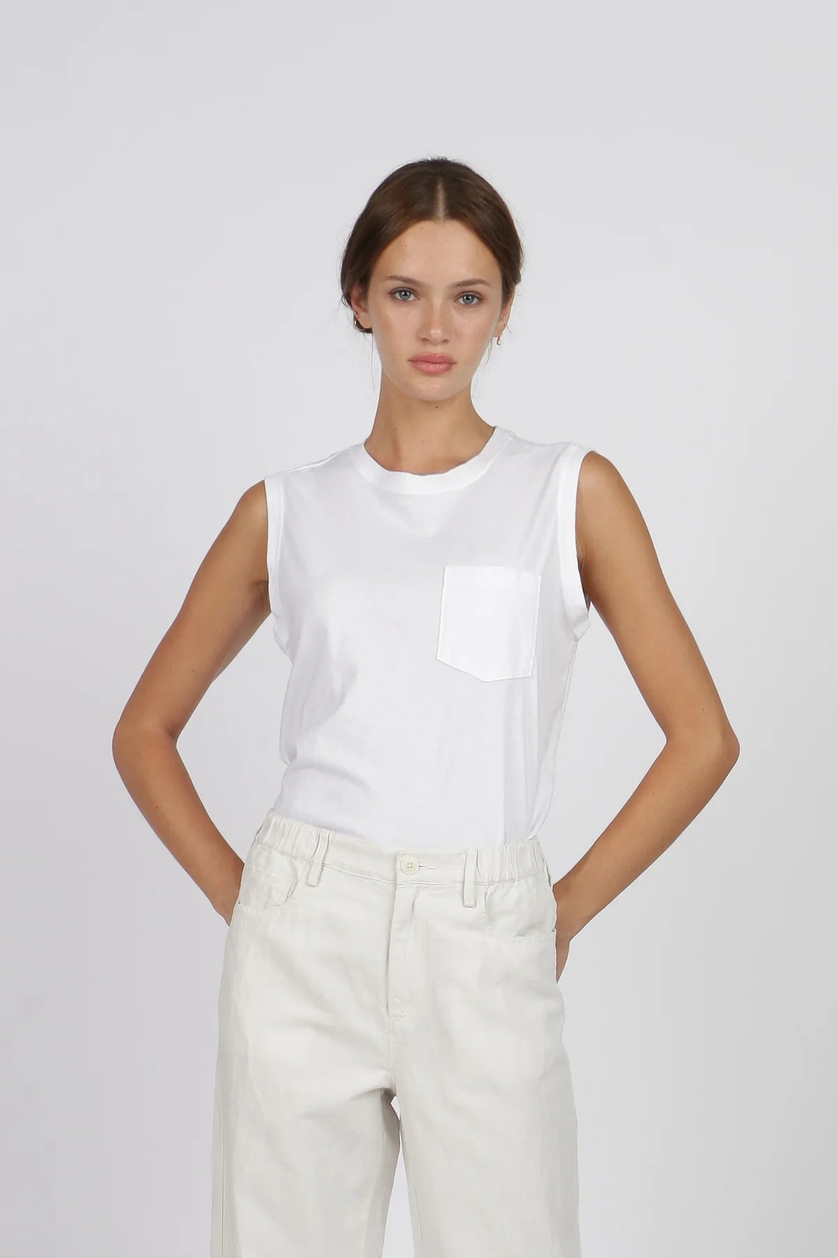 G1 Pocket sleeveless white tank top with chest pocket, worn by model in minimalist studio setting.